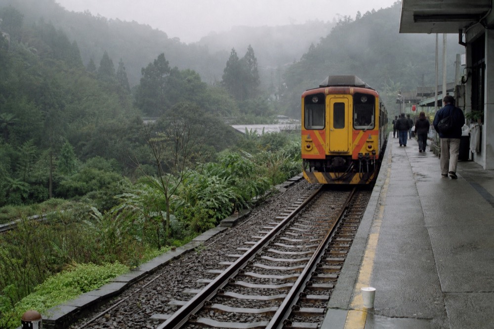 A single-car branch line train waiting at a small rural station platform in the Pingxi valley