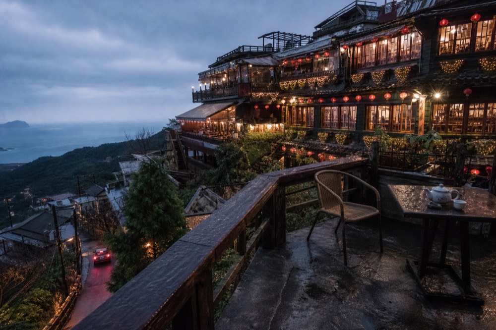 Dusk falling over teahouse balconies and warm lit windows above a dark sea horizon