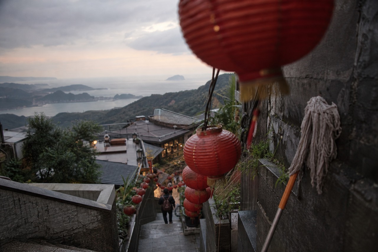 Lantern-lit stone steps and teahouse rooftops descending a hillside toward the sea in Jiufen