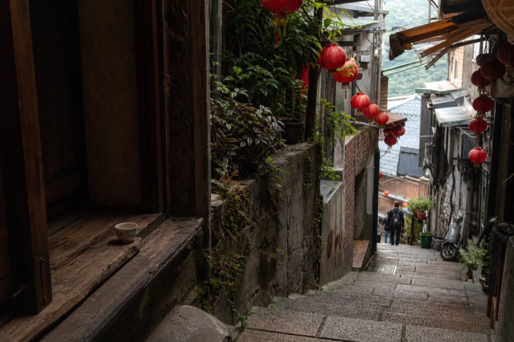 A narrow old street lined with red lanterns and shopfronts curving up a hillside