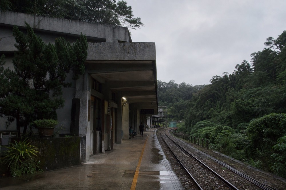 A railway platform beside a forested valley with a small station building and tracks curving away