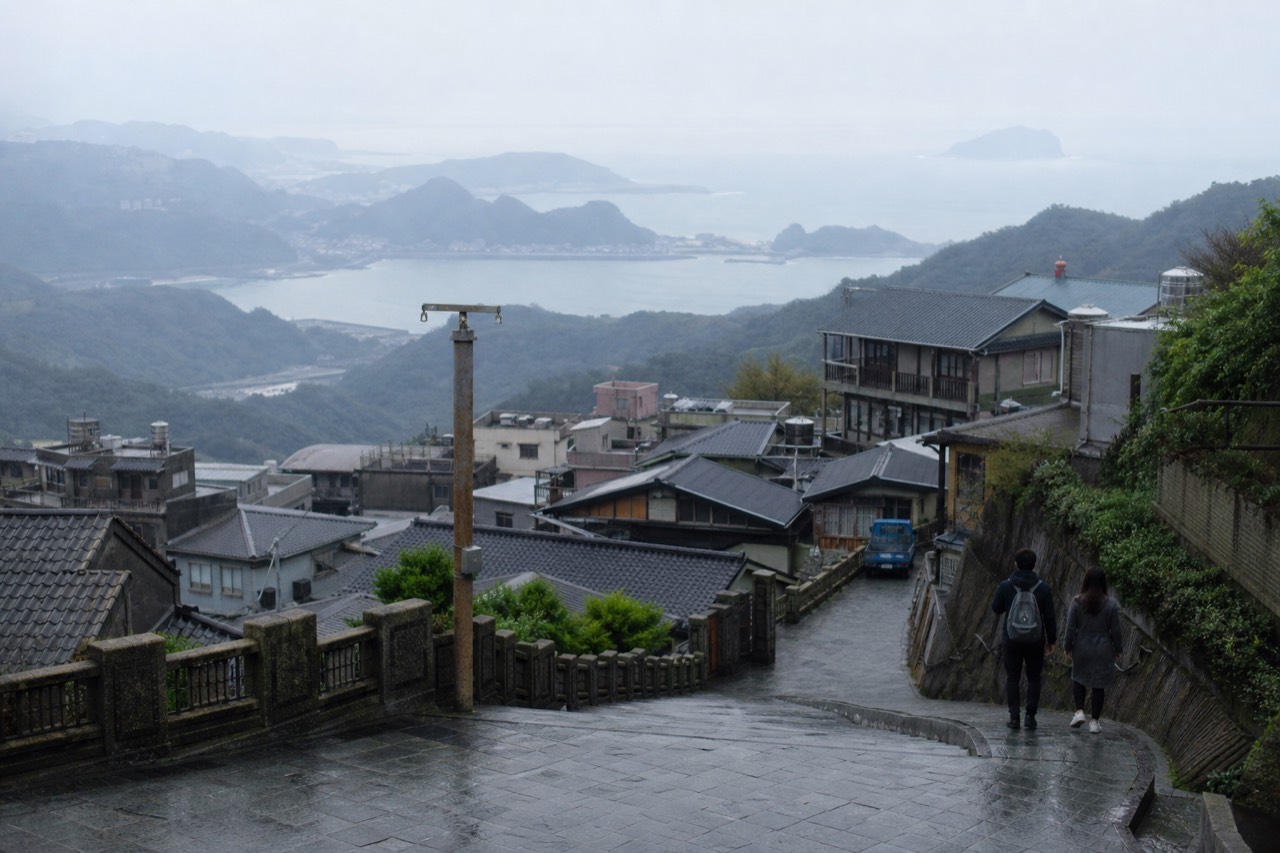 Mountain town rooftops descending toward a hazy coastline with the sea on the horizon