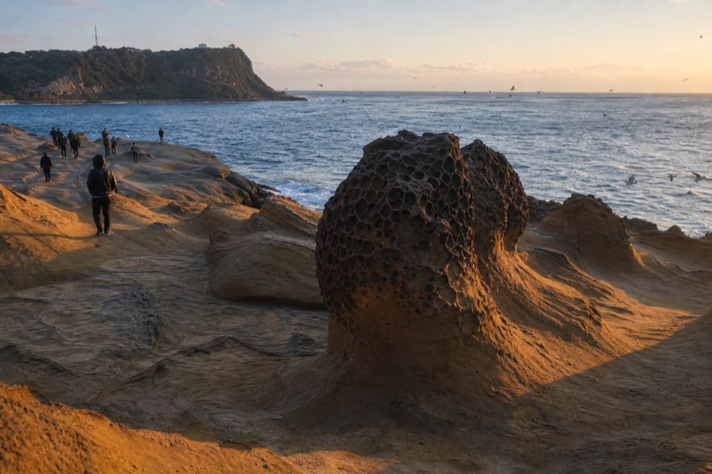 Sunset light over eroded rock formations and the sea beyond a coastal headland