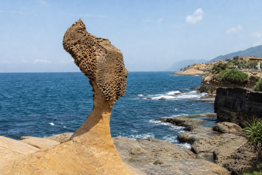 A slender mushroom rock with a profile resembling a queen's head viewed against the open sea