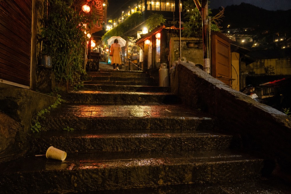 Warm light spilling from teahouse windows onto wet stone steps at night