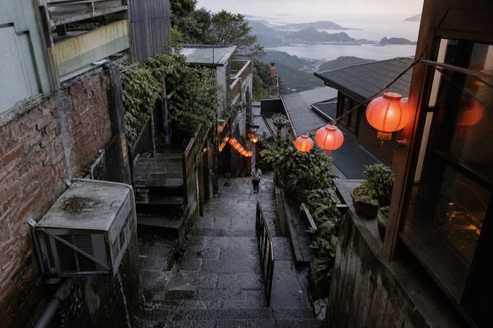 Steep stone stairway between old teahouses lit by red lanterns in the early evening