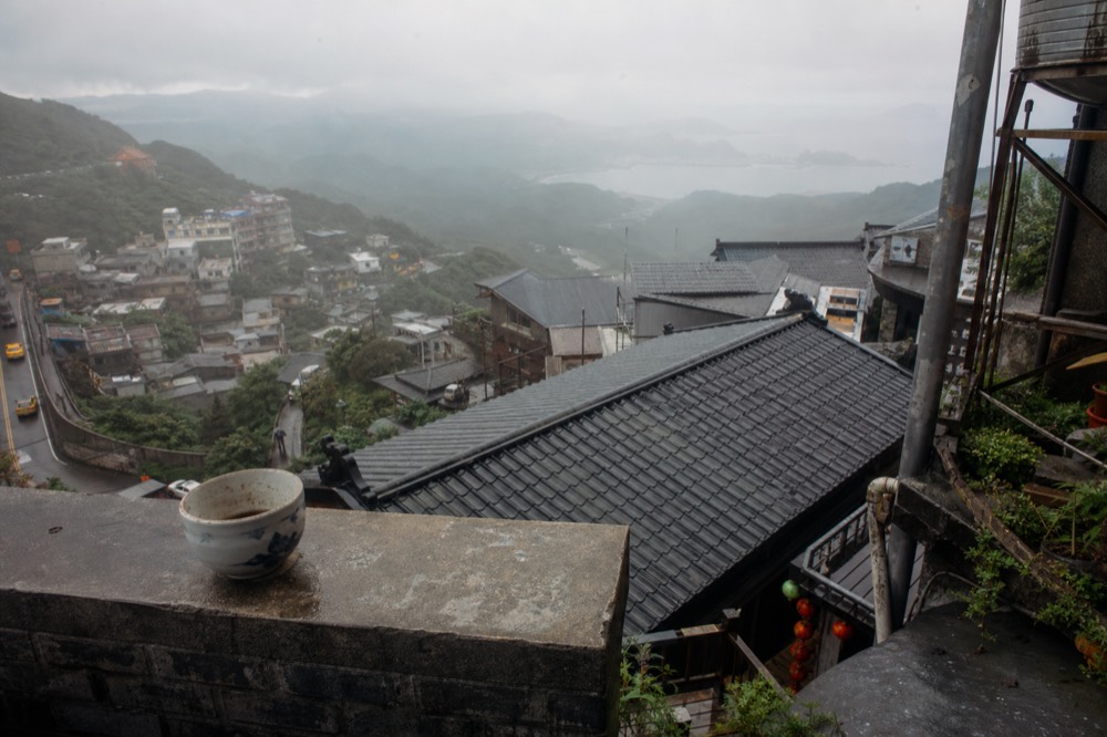 Morning mist over tiled rooftops descending toward the sea below a hillside town