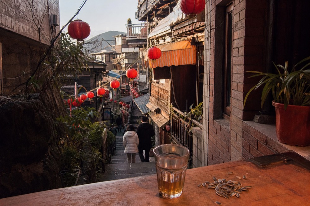 A narrow old street lane with red lanterns and shop signs in late afternoon light