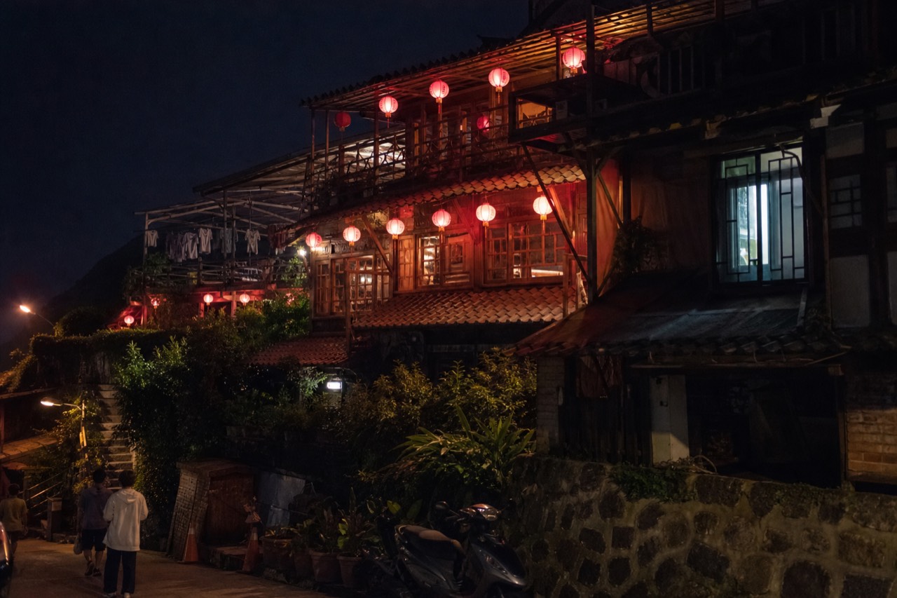 Red lanterns glowing above the rooftops of a hillside old street after dark