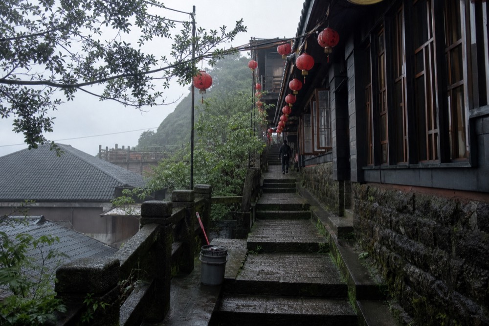 Steep stone stairway lane between old tea houses on a hillside, with red lanterns strung overhead
