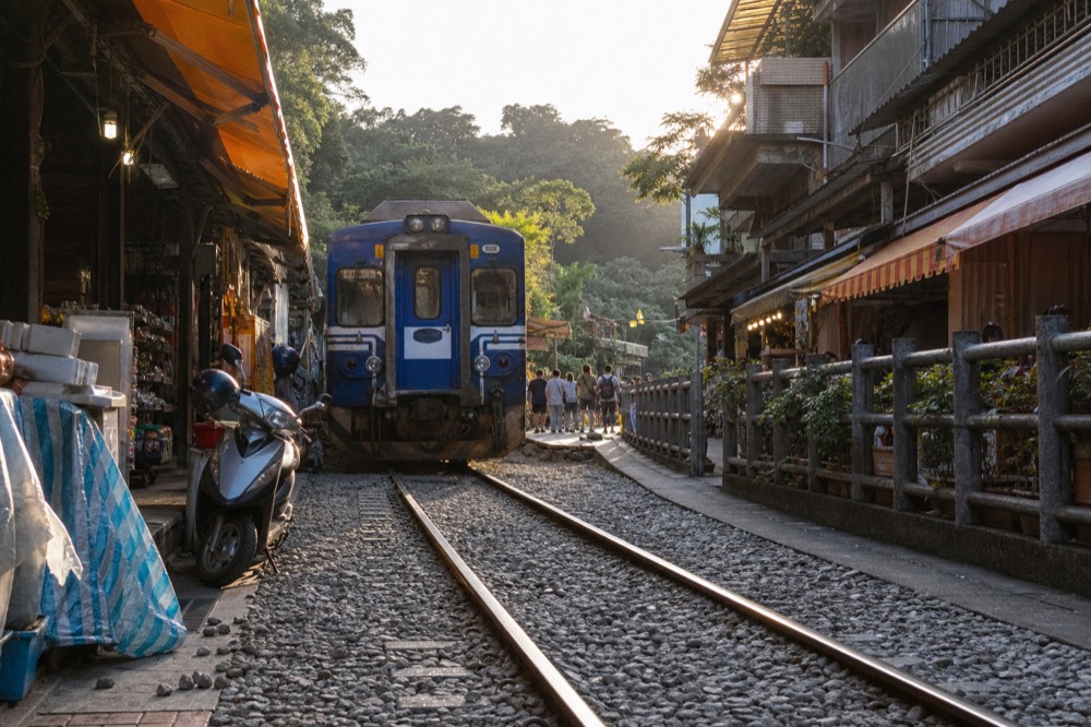 A single-car branch line train stopped on tracks running down the middle of a narrow old street between food stalls