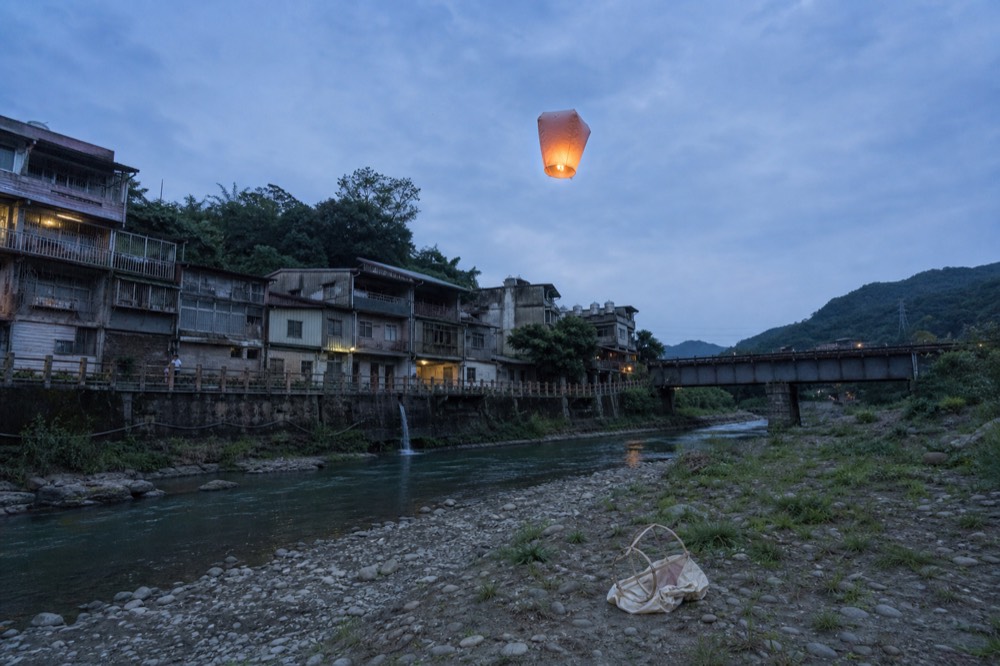 A sky lantern lifting off above a river gorge town with a railway bridge in the background
