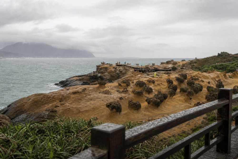 Coastal rock formations on a headland above a calm sea, seen from a walkway