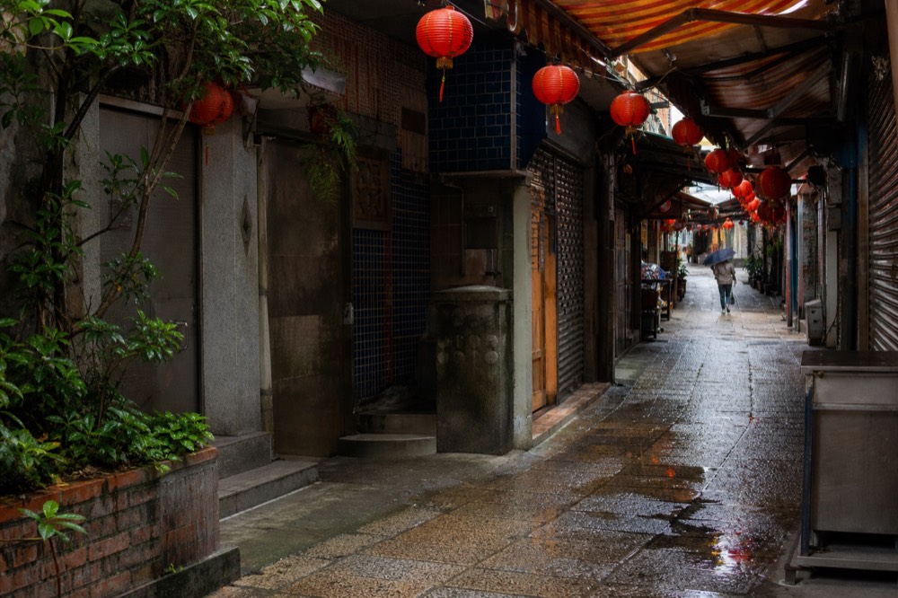 Lantern-lit stairway between old teahouse buildings on a hillside above the coast