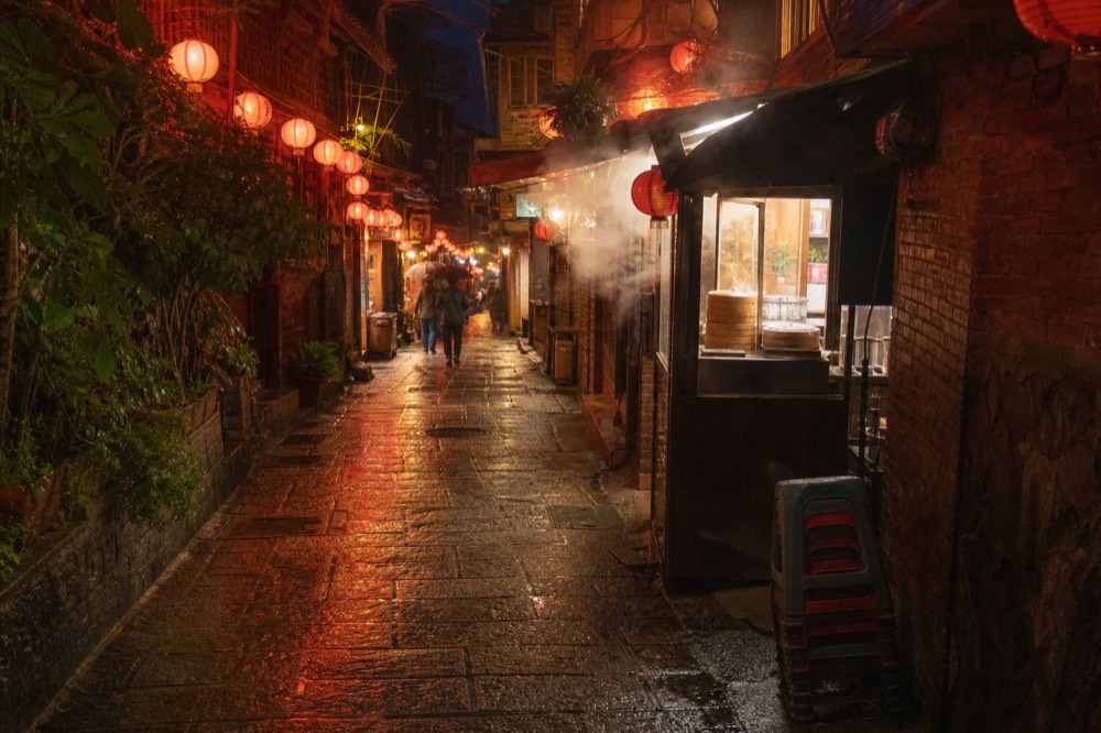 Narrow old street lane with red lanterns hanging over shopfronts on both sides