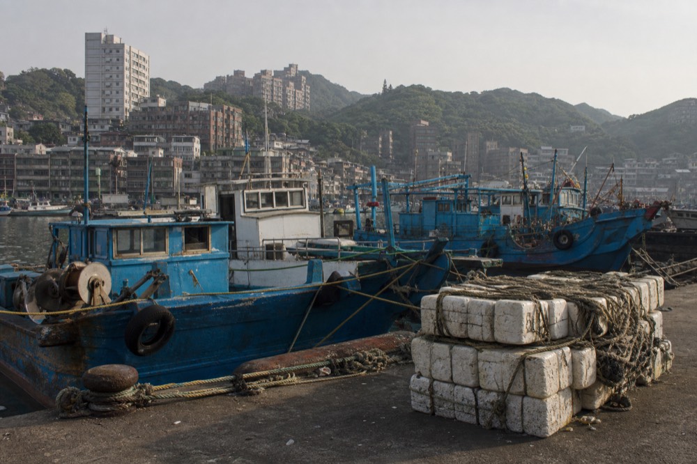 Fishing boats moored in a harbour with apartment buildings rising on the hillsides behind