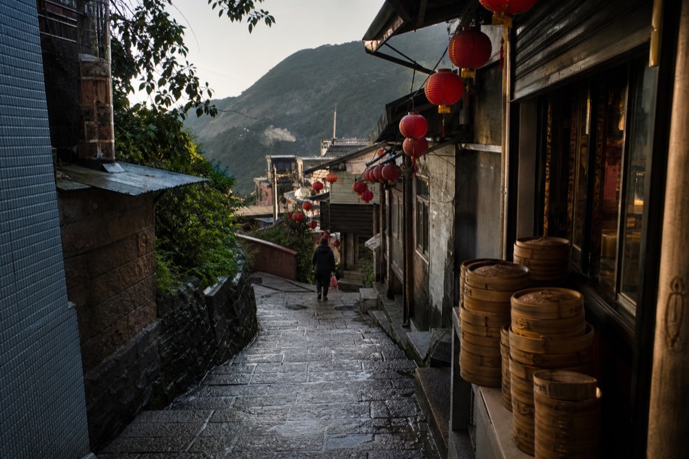 A narrow mountain street lined with lanterns and old shopfronts curving down a steep hillside