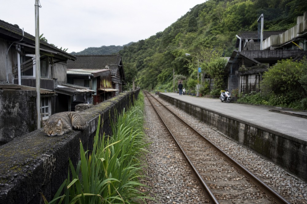 A single-track railway line running between old buildings in a narrow valley village