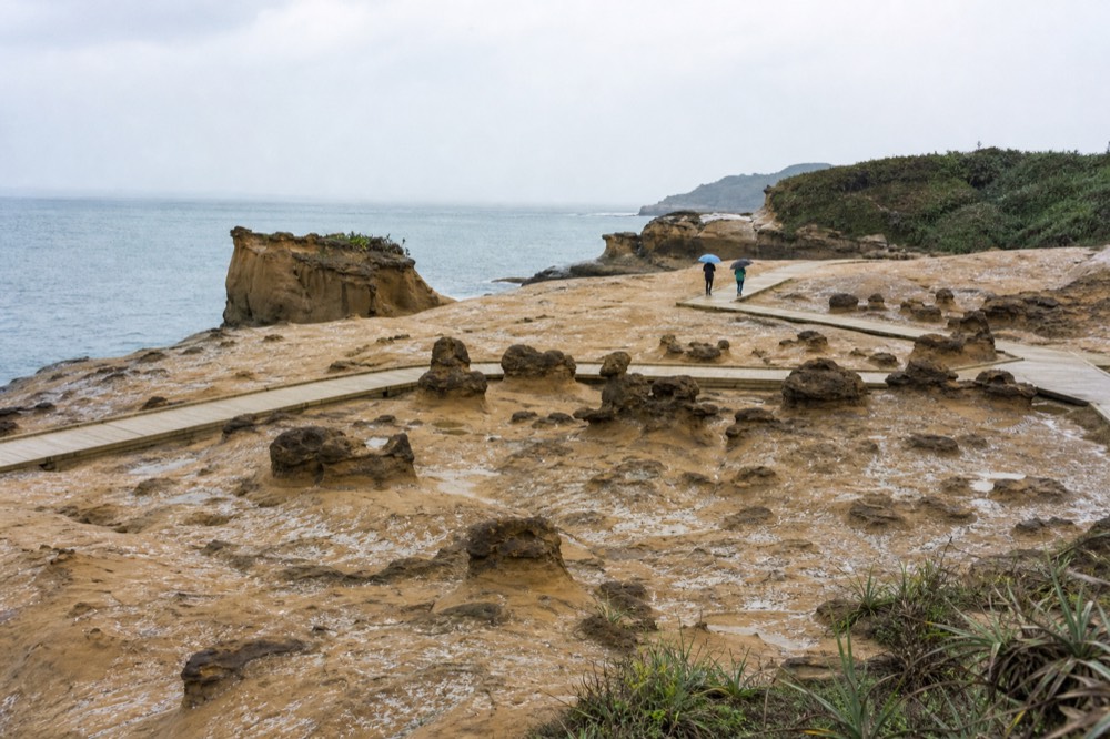 A coastal rock formation headland extending into a calm sea under an overcast sky
