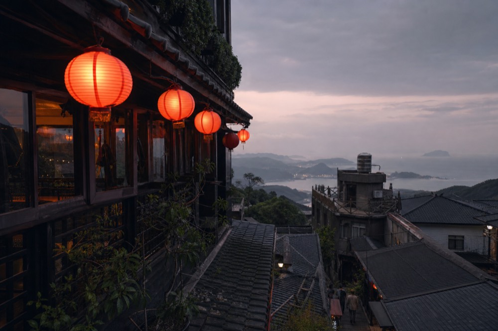 Teahouse balconies with red lanterns stacked on a steep hillside above the sea at dusk
