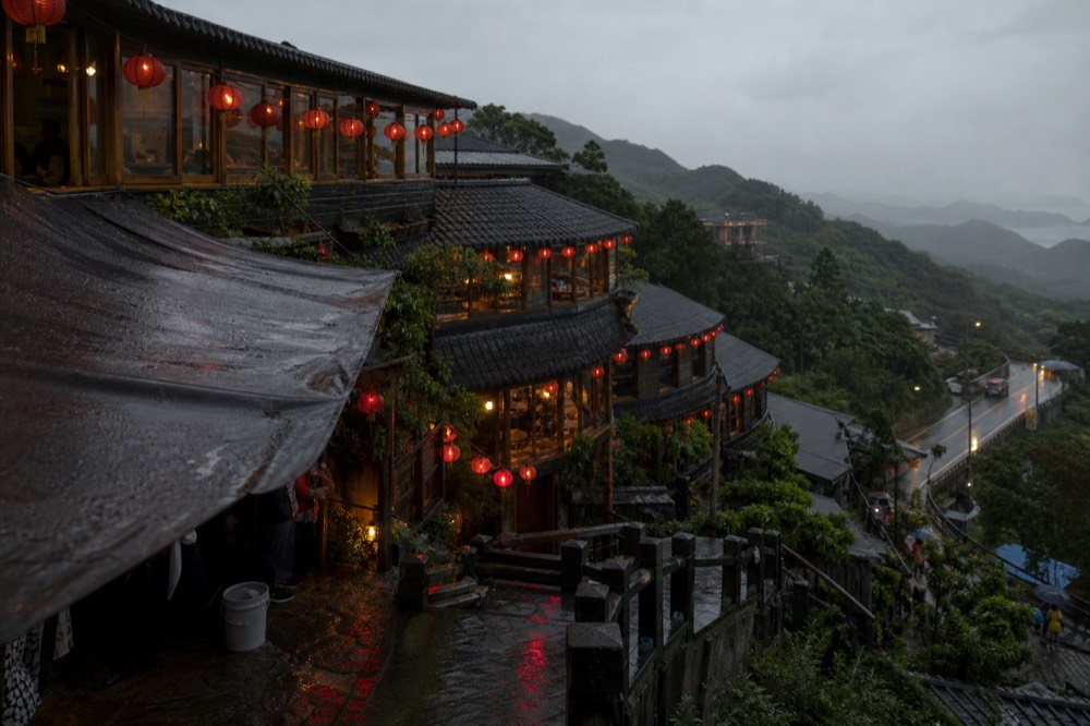 Red paper lanterns glowing above the rooftops of a hillside old street at dusk