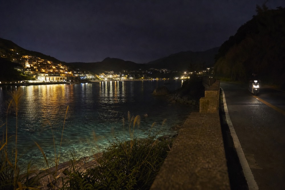 Lights of a hillside town reflected over a dark harbour at night