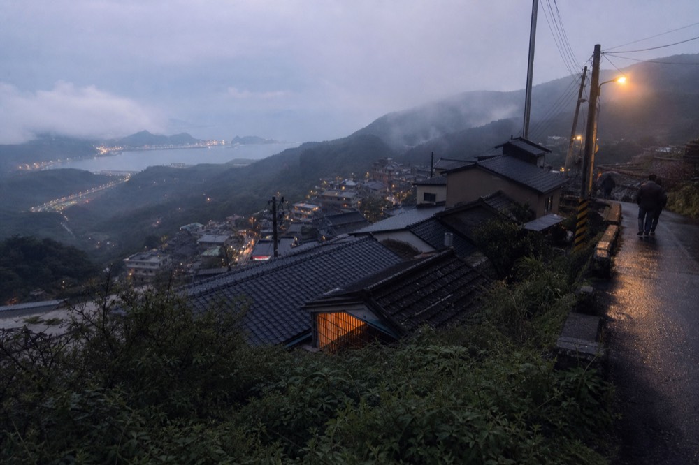 Coastal mountain town at dusk with lit windows above the sea