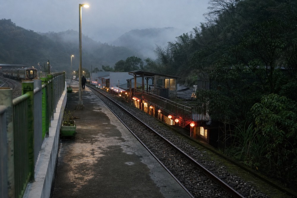 A hillside town at dusk with warm lantern light along a narrow street below misty slopes