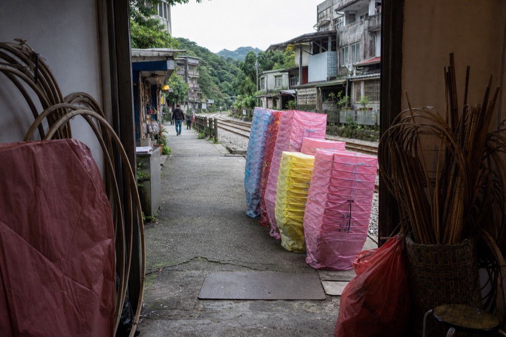 Colourful paper lanterns stacked beside a shopfront on an old street with railway tracks