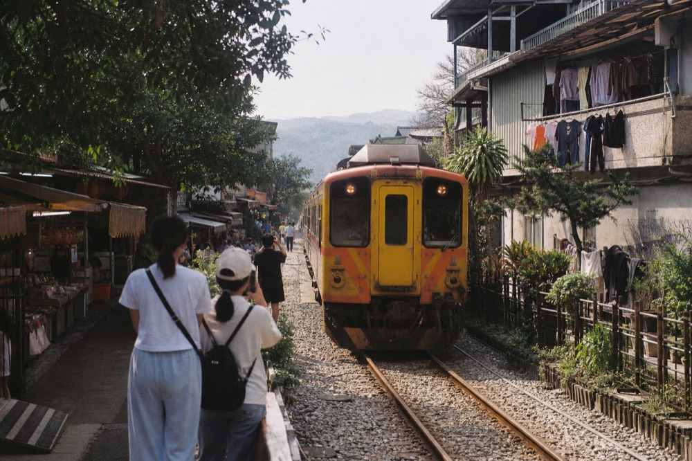 A train passing slowly along tracks that run between shopfronts on a narrow old street
