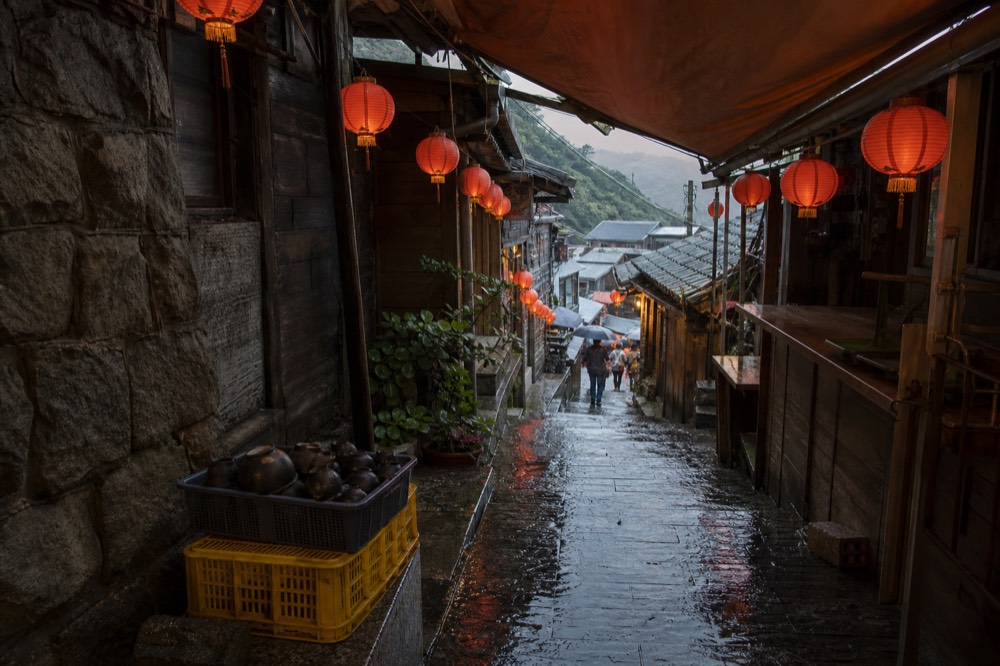 A narrow stone street between old tea houses, wet flagstones reflecting red lantern light