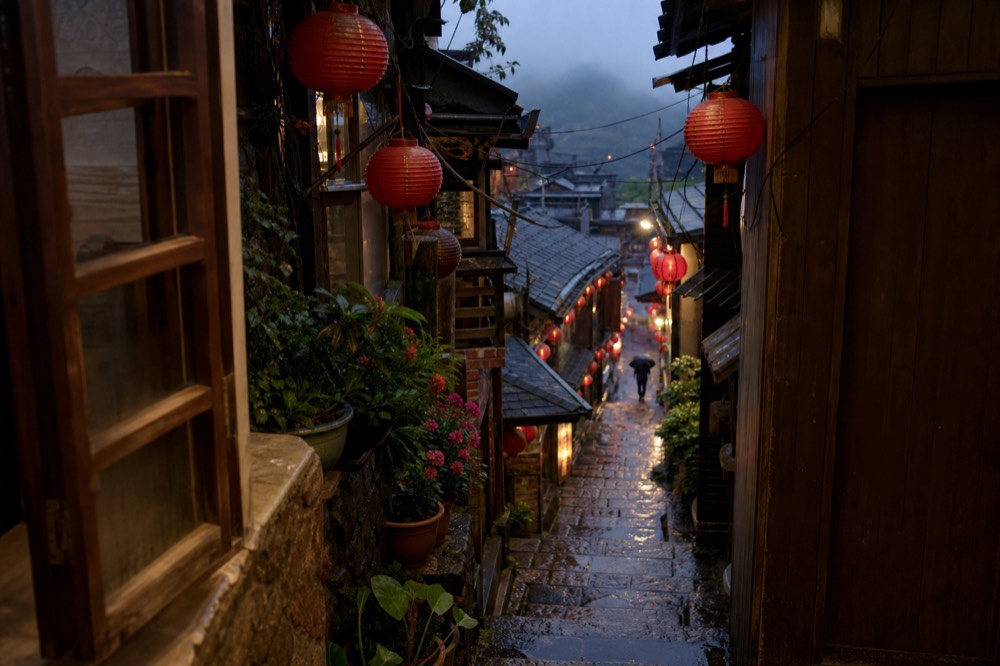 Narrow stone lane in a hillside town with red lanterns hanging overhead and old shopfronts on both sides