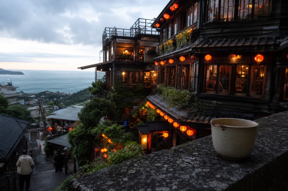 Old wooden teahouse with lit windows on a hillside above the sea at dusk