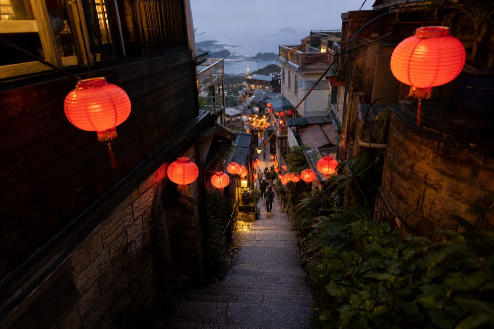 Red lanterns strung across a narrow old street with stone steps and shopfronts in evening light