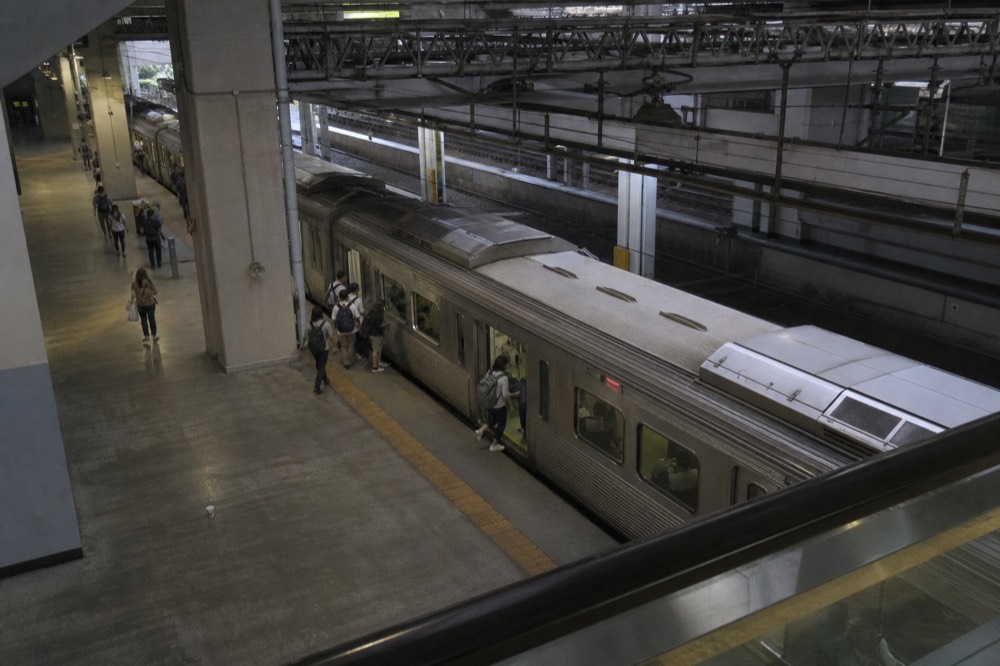 A busy city railway platform in Taipei with a train boarding passengers in the morning