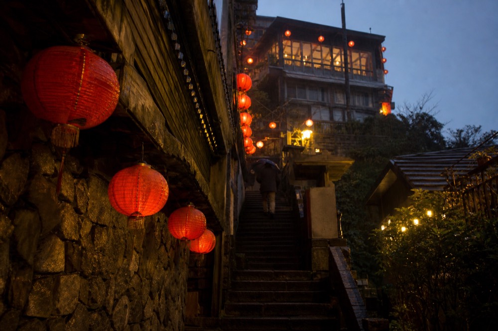 The Shuqi Road staircase at night, lined with glowing red lanterns, leading up to a traditional teahouse with warm yellow lights.