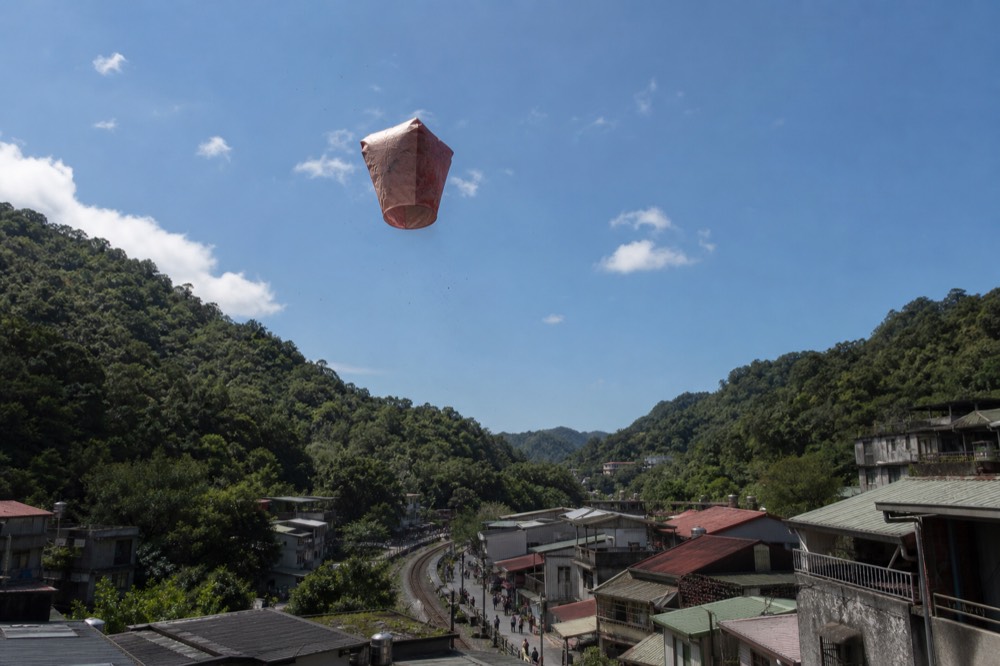 A lantern floating above a river valley between forested hills