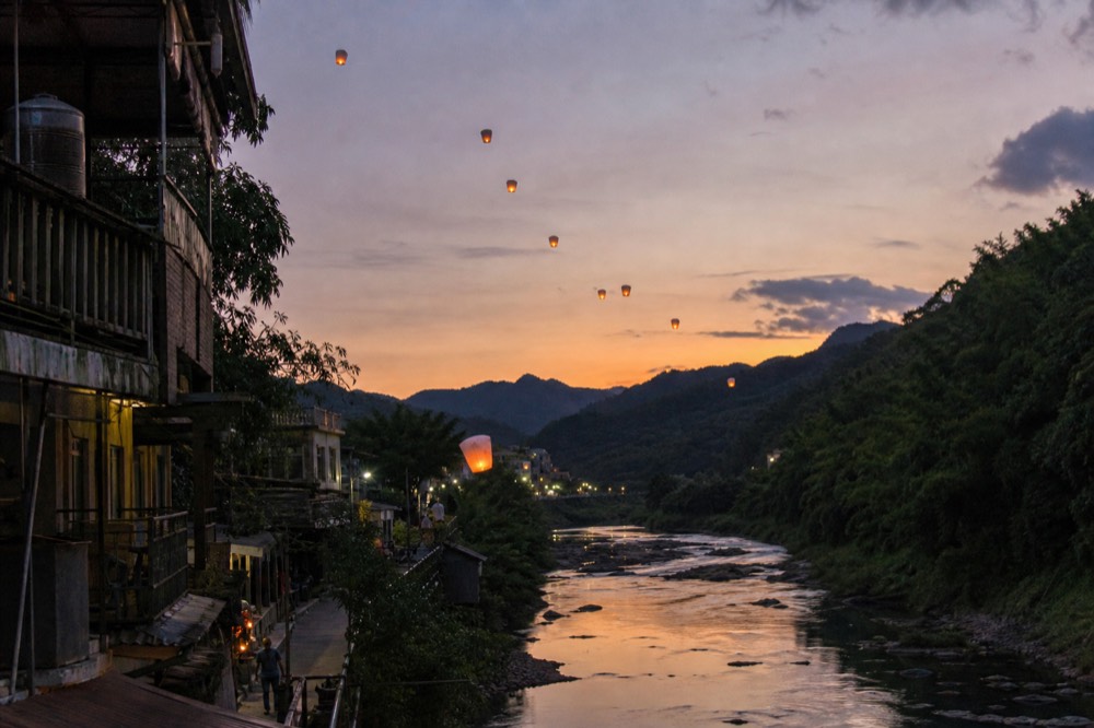 Lanterns drifting in a line above a river valley at dusk