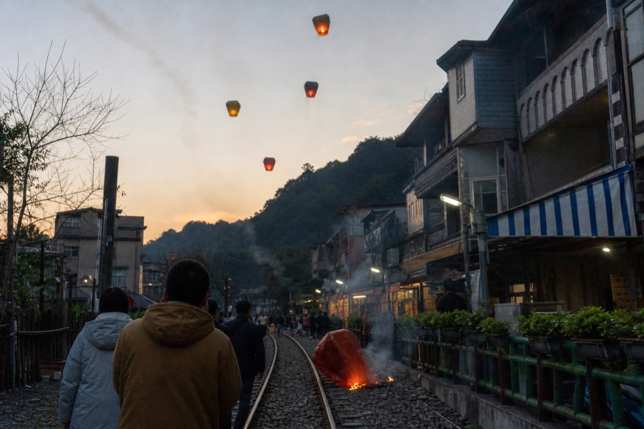Sky lanterns rising above a mountain village street at dusk