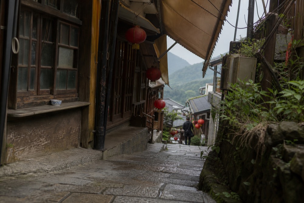 Weathered wooden storefronts and red lanterns along a narrow stepped lane in an old mining town
