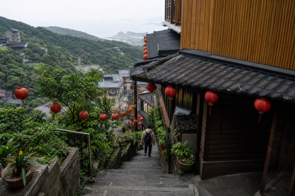A steep stone stairway between tall old buildings with red lanterns strung overhead