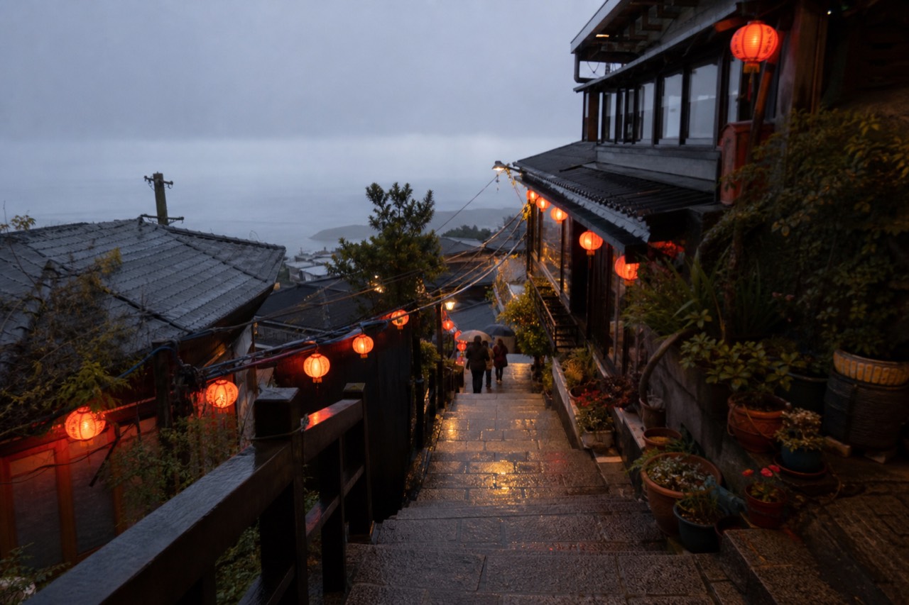 Lantern-lit stone steps climbing between old teahouse buildings on a hillside above the sea