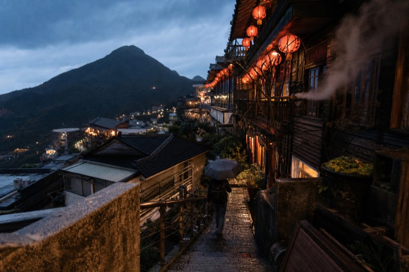 Lanterns glowing above a narrow Jiufen lane at dusk, warm light on stone steps and teahouse balconies in Taiwan