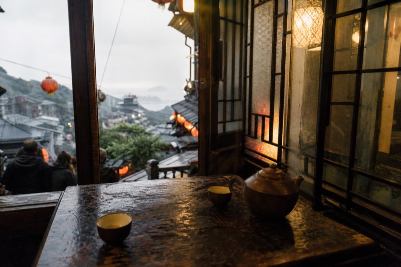 A teahouse interior in Jiufen with wooden tables and small tea pots, lantern light through the window in Taiwan