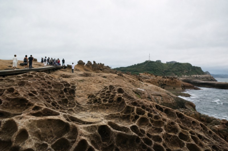 Rock formations on a headland above the sea in northern Taiwan, with visitors walking the paths above the water