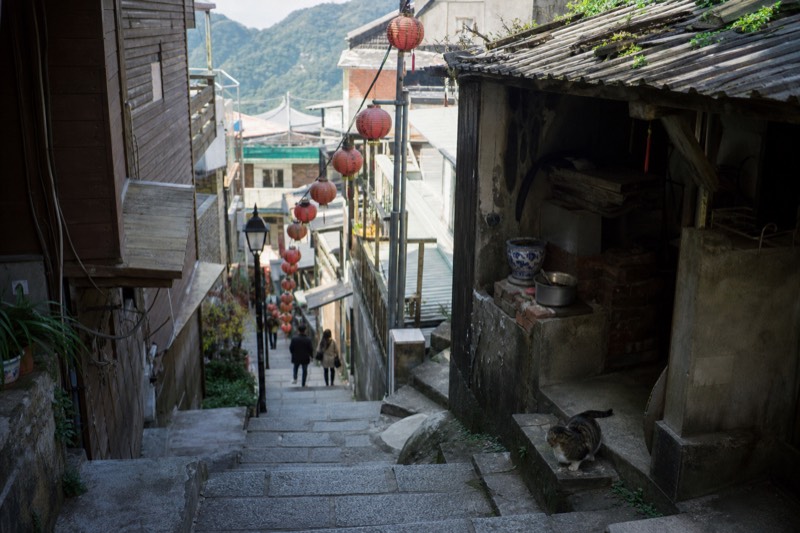 A stone stairway lane in Jiufen lined with old-style shopfronts, lanterns hanging above the passage in Taiwan