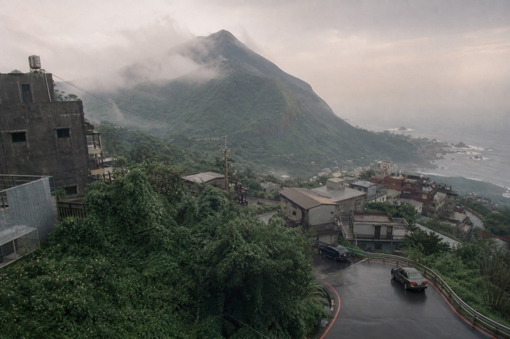 A coastal valley view from a hillside town under a clearing afternoon sky