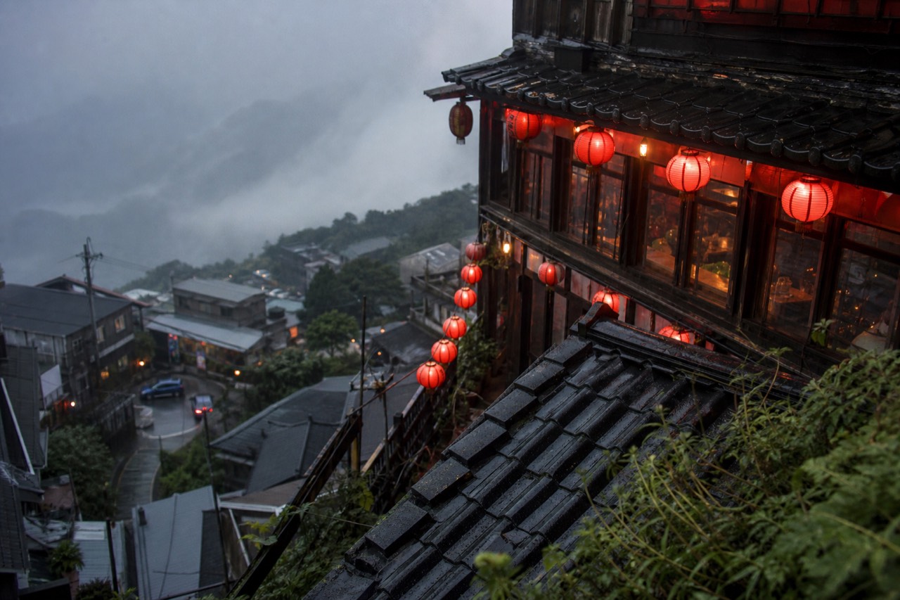 Red lanterns and steep rooftops of a mountain town under low coastal clouds