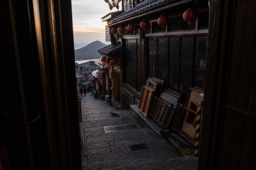 An early morning old street nearly empty, lanterns unlit above closed shopfronts