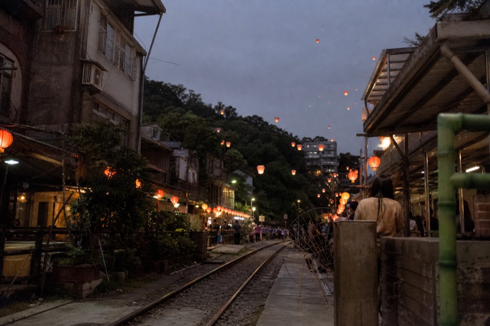 Red paper lanterns hanging in rows above a stone street at dusk